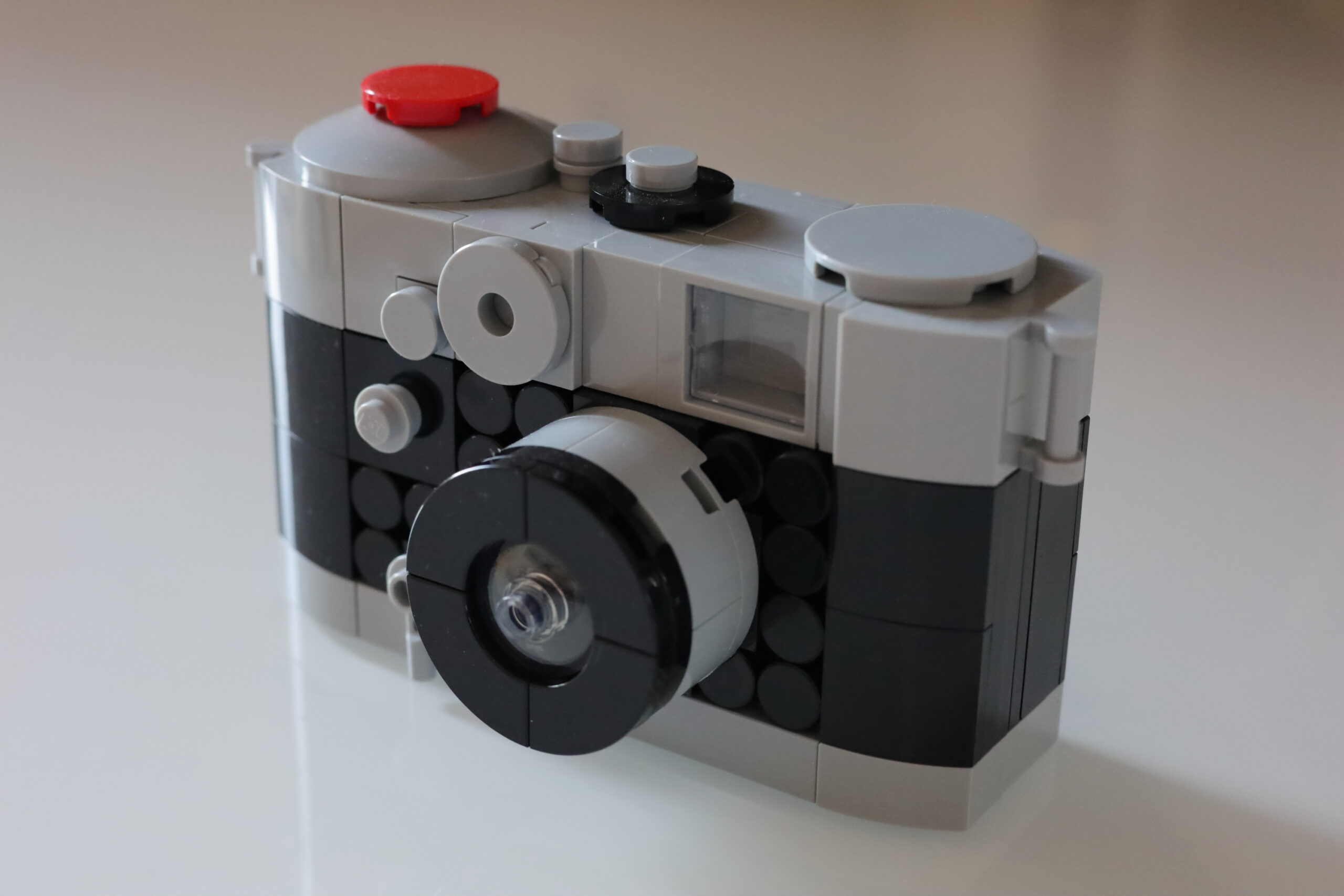 Das Bild zeigt eine Kamera aus Lego. Sie ist oben und unten grau und in der Mitte schwarz. der Auslöser ist rot.